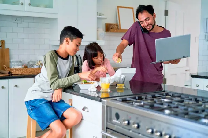 Father with laptop feeding kids with take out food in kitchen