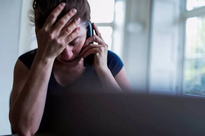 Frustrated woman talking on telephone at laptop