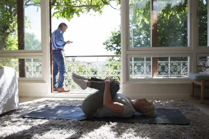 Senior woman stretching on yoga mat at summer balcony doorway