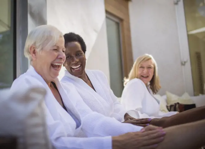 Happy women friends in spa bathrobes laughing on patio