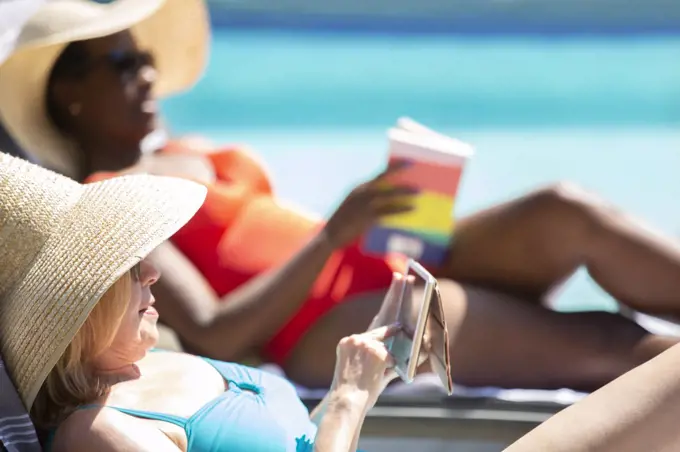 Senior woman using smart phone and sunbathing at summer poolside