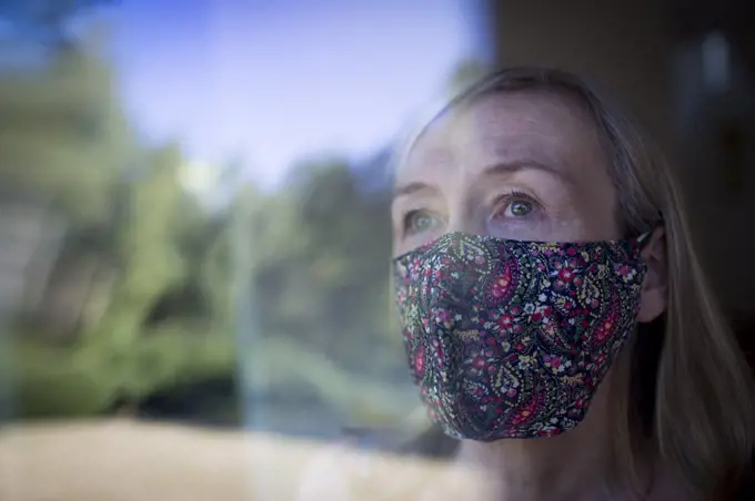 Worried senior woman in face mask at window
