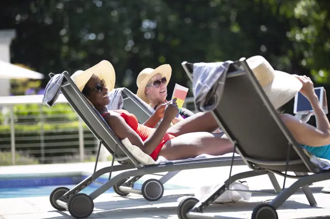 Happy senior women friends sunbathing at sunny summer poolside