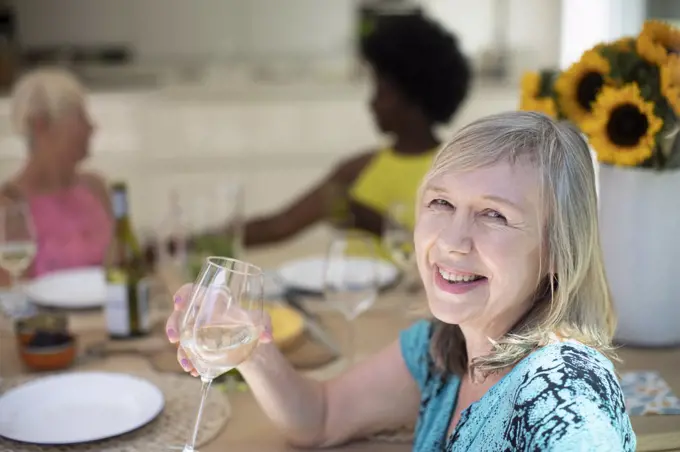 Portrait happy senior woman drinking white wine with friends at table