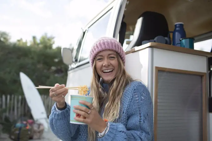 Portrait happy young woman eating instant noodles at camper van