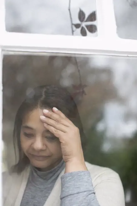 Depressed woman standing at window with head in hands
