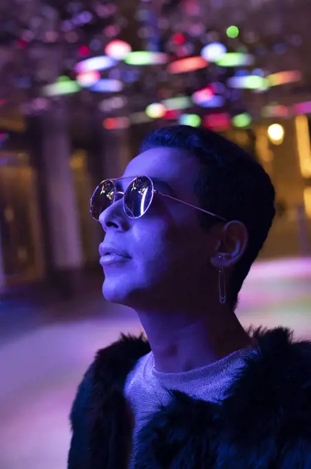 Portrait stylish young man in sunglasses looking up at neon lights