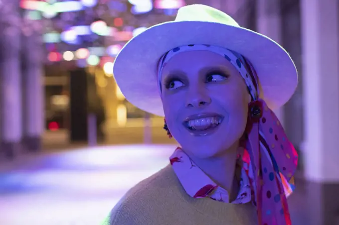 Portrait happy stylish woman in headscarf and fedora under neon light