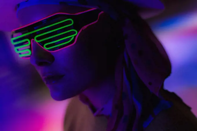 Close up stylish woman wearing neon sunglasses in dark