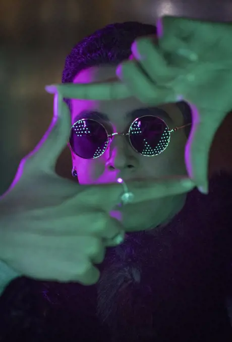 Portrait cool young man in sunglasses forming finger frame in neon