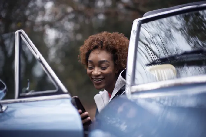 Happy young woman using smart phone at convertible