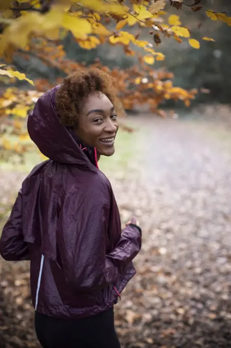 Portrait happy young woman jogging in autumn park