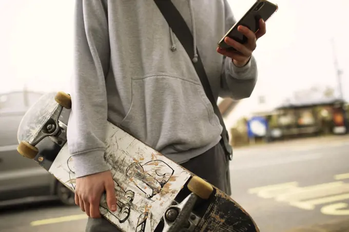 Close up teenage boy with skateboard and smart phone on street