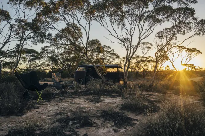 Camping chairs and parked van in Australian bush at sunset
