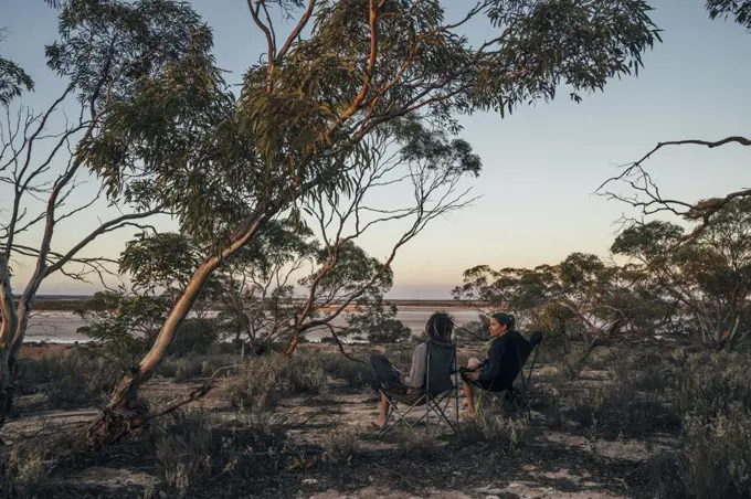 Couple relaxing in camping chairs among trees, Australia