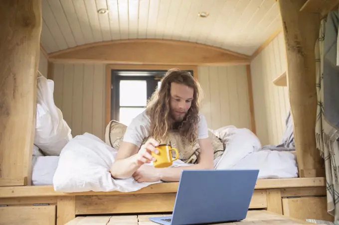 Young man relaxing with coffee and laptop in tiny cabin rental