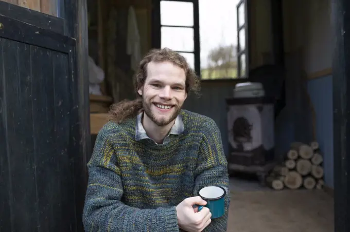 Portrait happy young man drinking coffee in cabin doorway