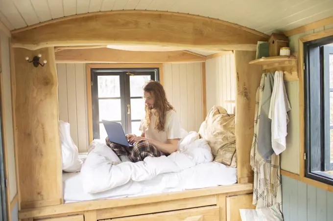 Young man using laptop in tiny cabin rental bed