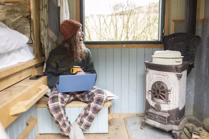 Thoughtful young man using laptop in tiny cabin rental