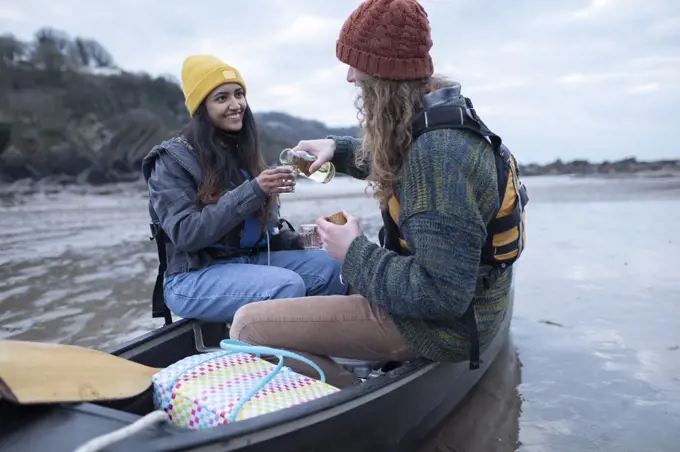 Happy young couple drinking wine in canoe on beach