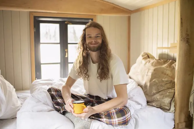 Portrait happy young man in pajamas drinking coffee in bed