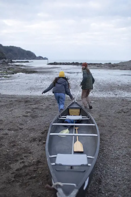 Young couple pulling canoe on beach