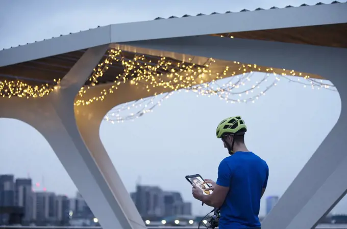Man in helmet using digital tablet below illuminated bridge, London