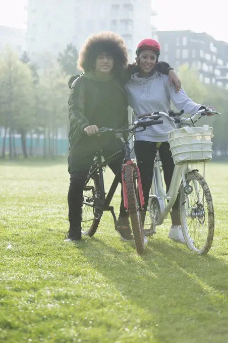 Portrait happy teen couple on bicycles in urban park grass