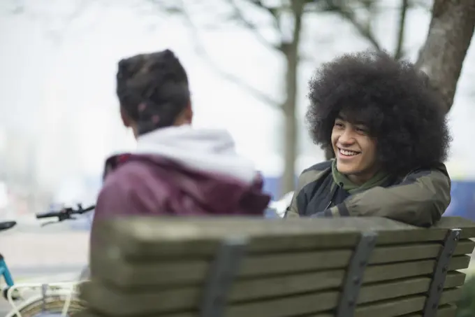 Happy young man with afro talking to friend on park bench