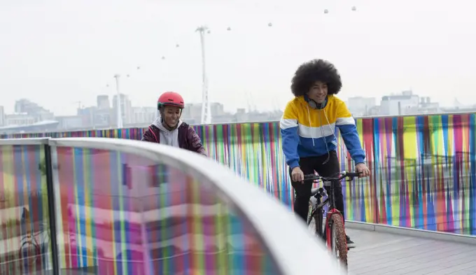Teen friends riding bicycles on modern footbridge in city, London, UK