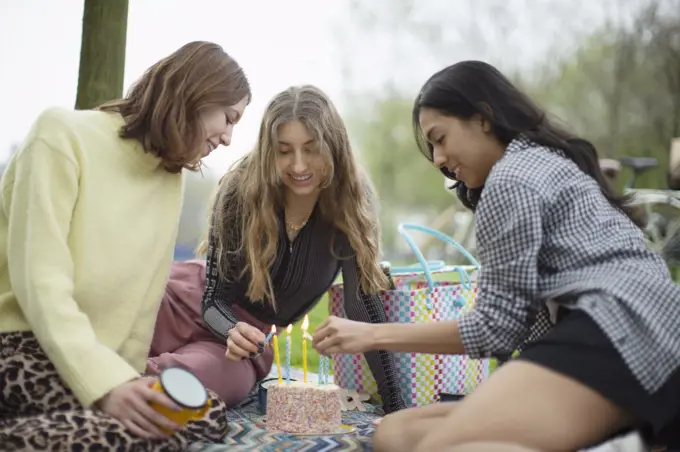 Young women friends celebrating birthday with cake in park