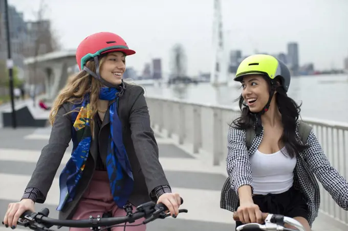 Happy young women friends in helmets riding bicycles in city