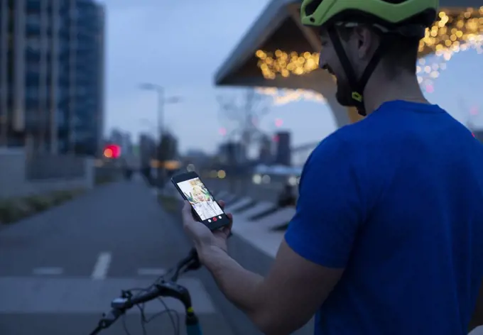 Man on bicycle video chatting with smart phone in city at night