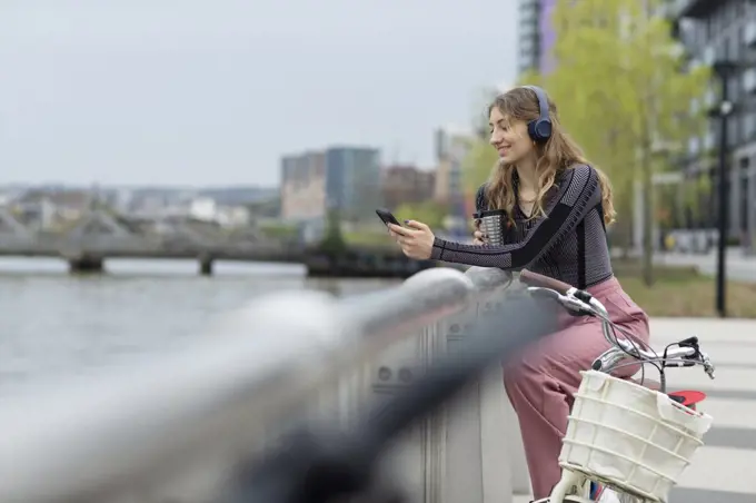 Young woman with headphones using smart phone at urban waterfront