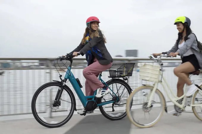Young women friends riding bicycles on urban bridge