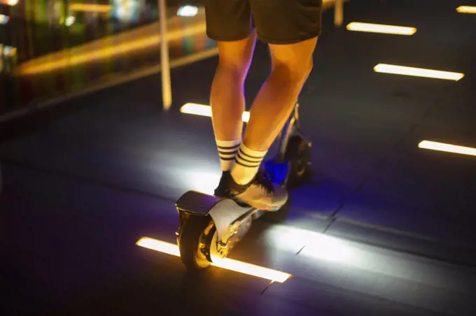 Man riding scooter on illuminated sidewalk at night
