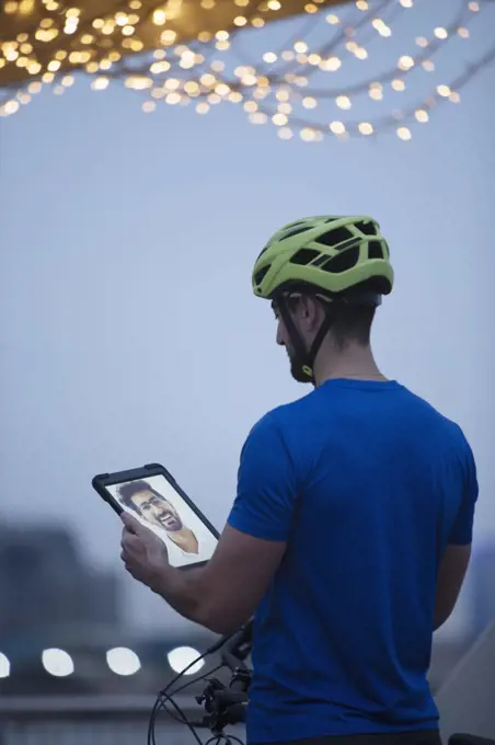 Man in bike helmet video chatting with friend on digital tablet screen