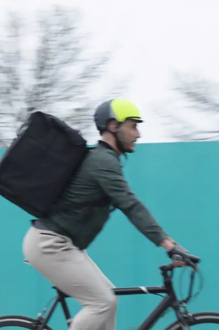Male courier riding bicycle with delivery bag