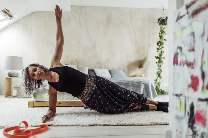 Senior woman exercising in side plank on bedroom rug