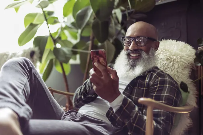 Happy senior man using smart phone in armchair