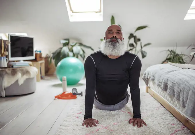 Mature man with beard practicing yoga upward facing dog at home