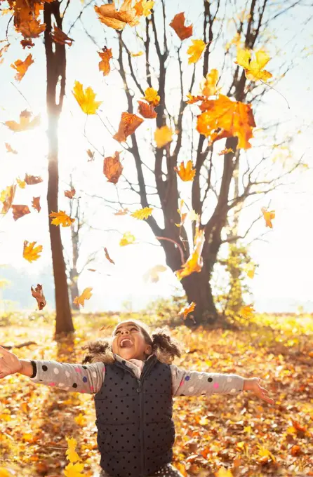 Playful girl throwing leaves overhead in sunny autumn park