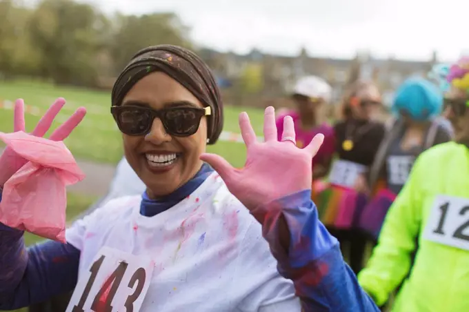 Portrait enthusiastic female runner with pink holi powder hands at charity run