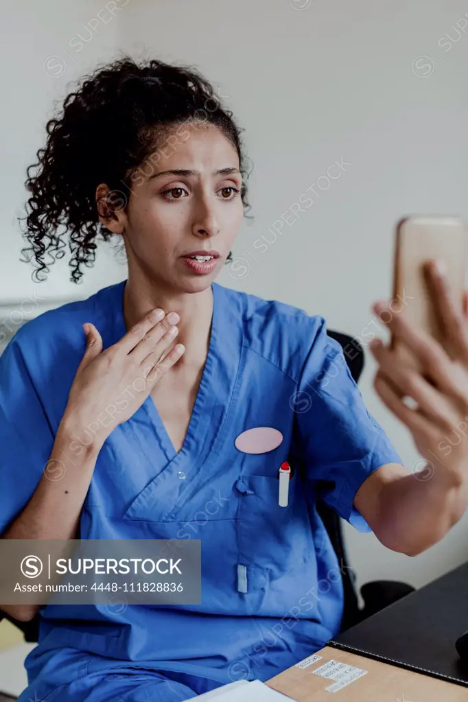 Worried nurse explaining on video conference while sitting in hospital