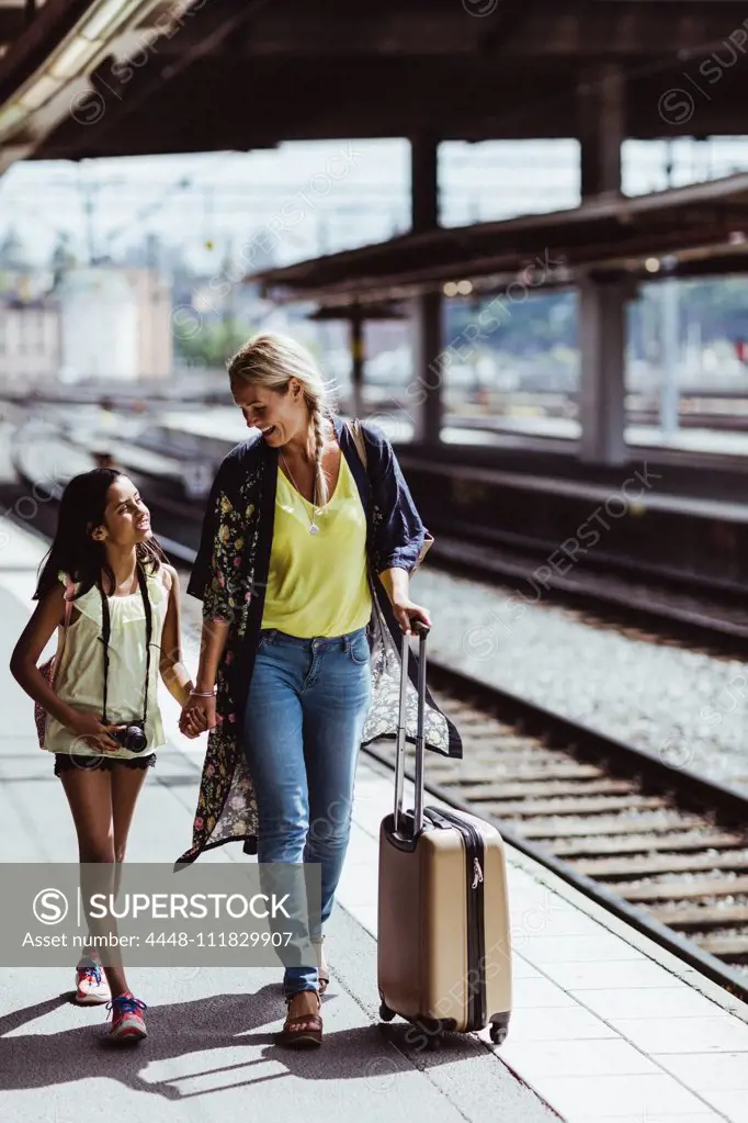 Smiling mother and daughter with luggage talking while walking at station