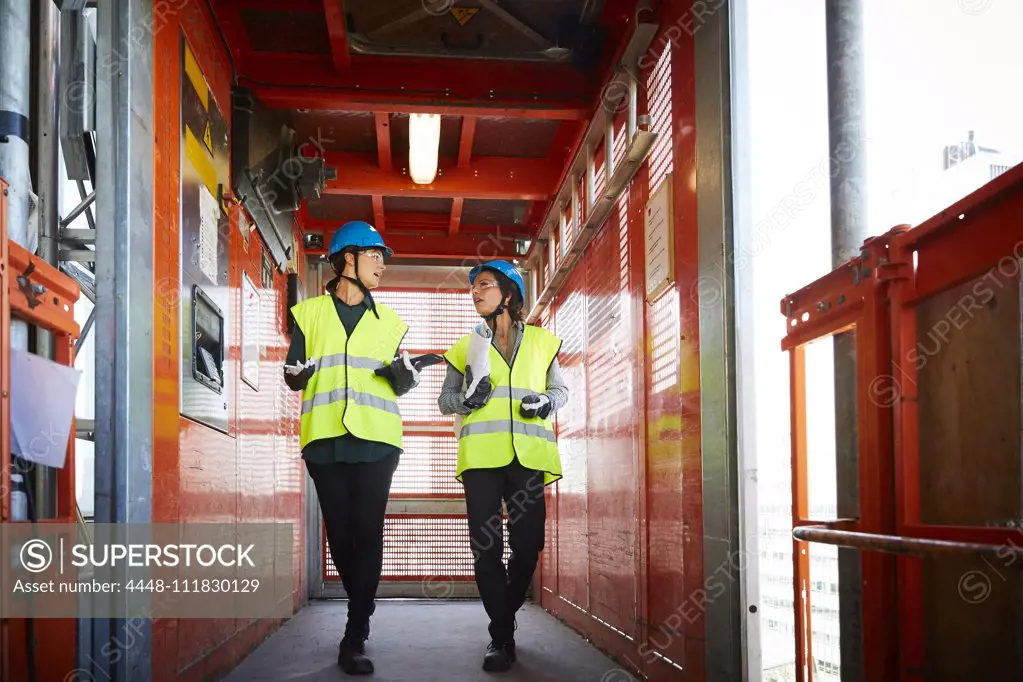 Full length of female engineers discussing while walking in freight elevator at construction site