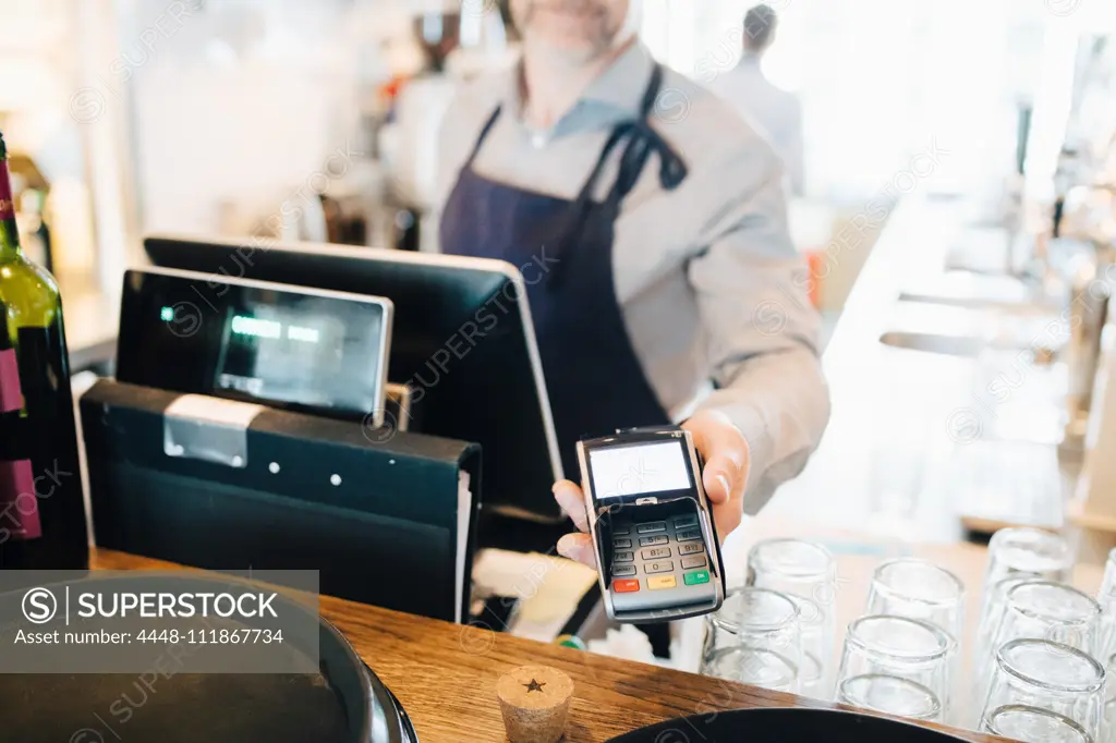 Midsection of man holding credit card reader in restaurant