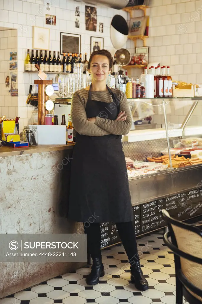 Portrait of confident young female owner standing with arms crossed at cafe