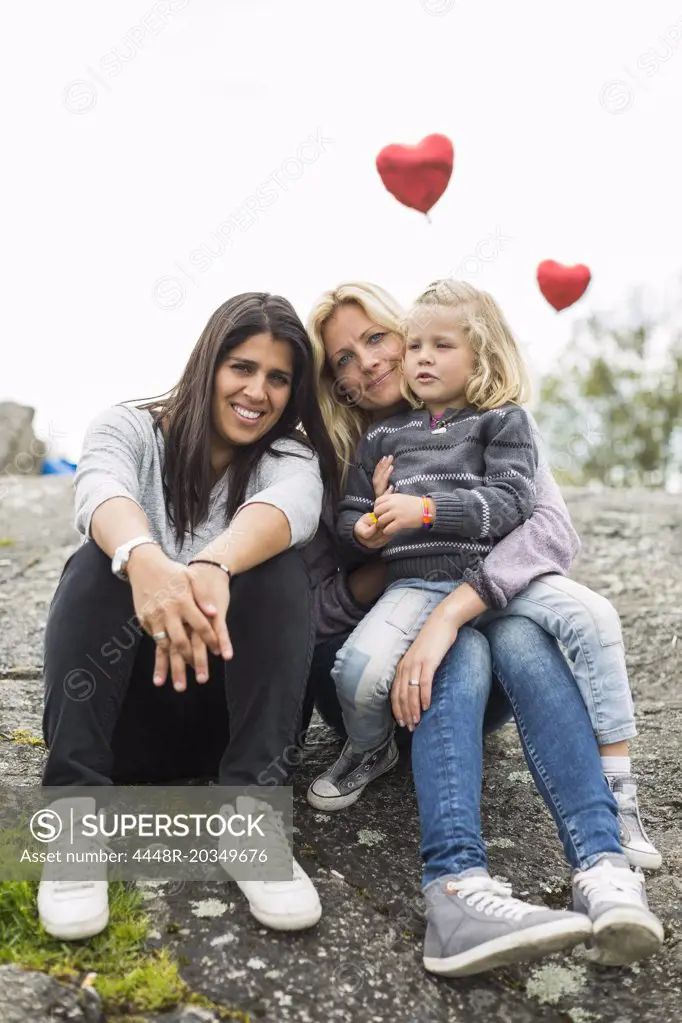 Portrait of happy female homosexual family relaxing on rock