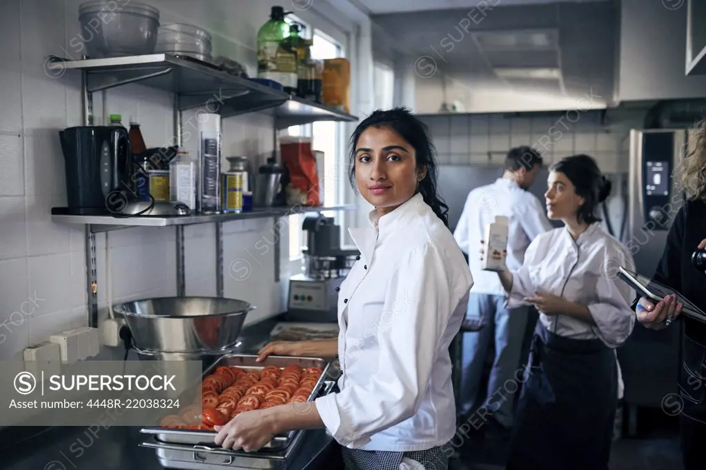 Portrait of chef with tomatoes in baking sheet at commercial kitchen